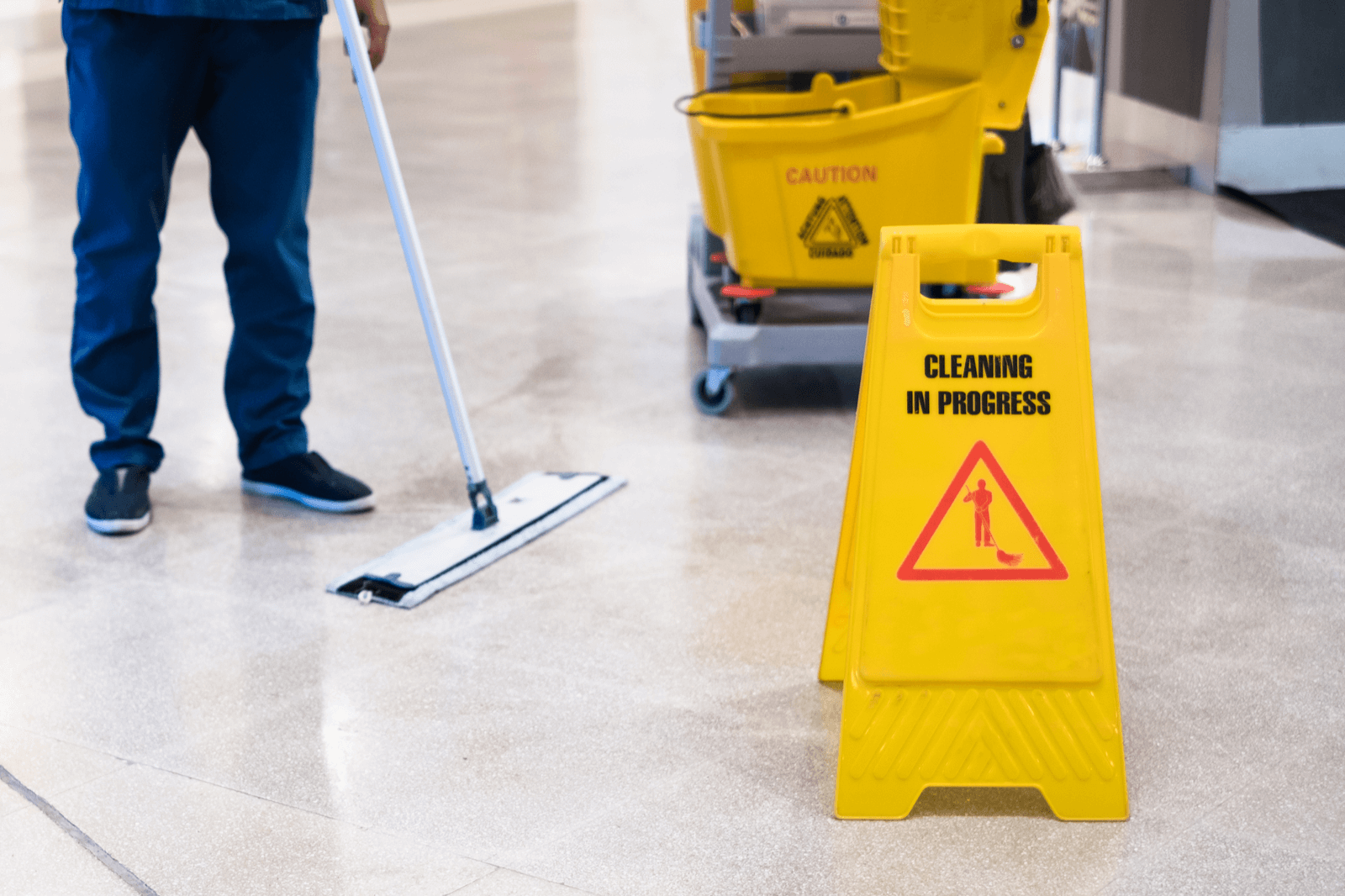 Person cleaning a hard tile floor with warning sign in place