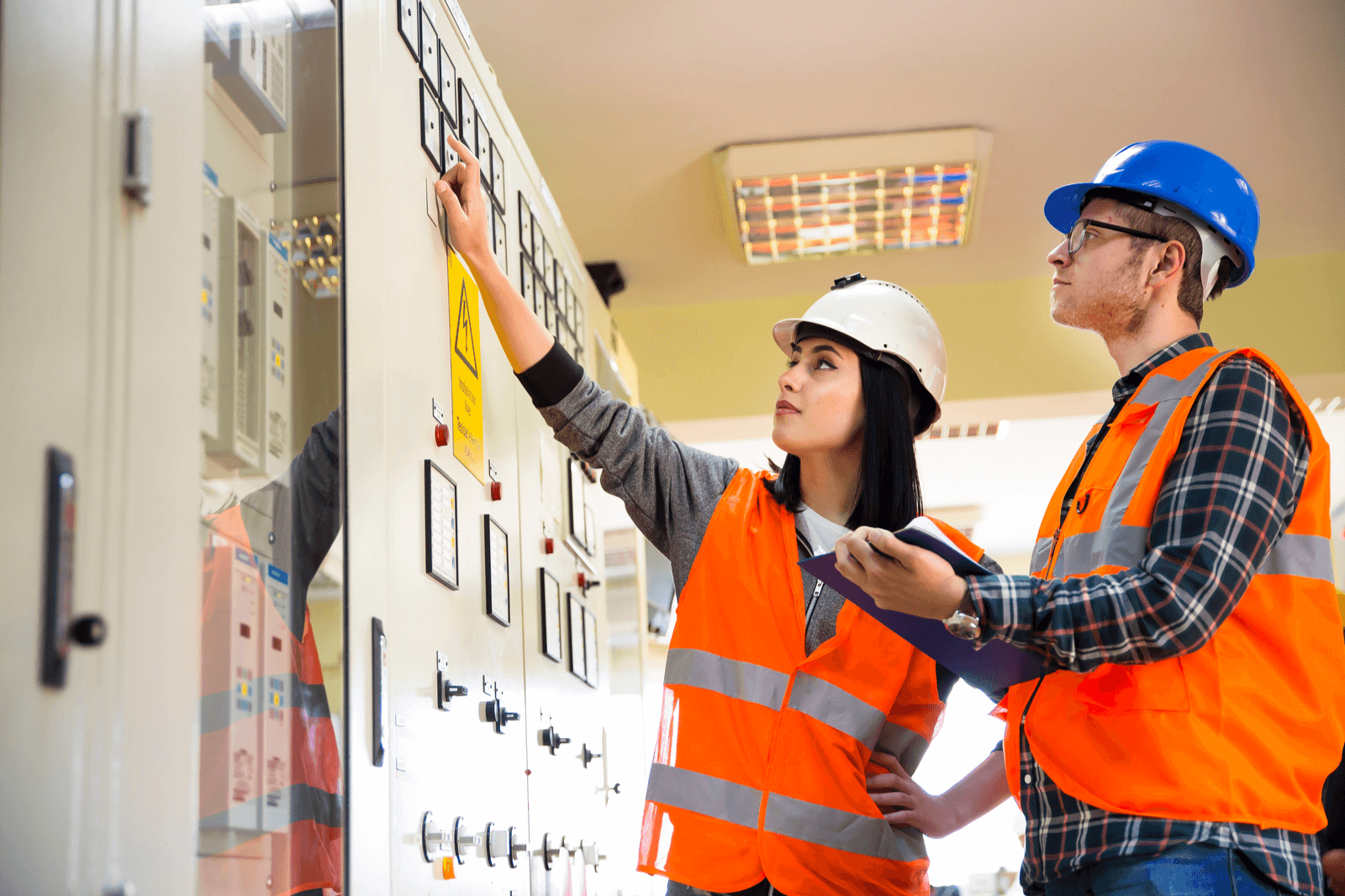 two people in hardhats looking at electrical meter on a panel